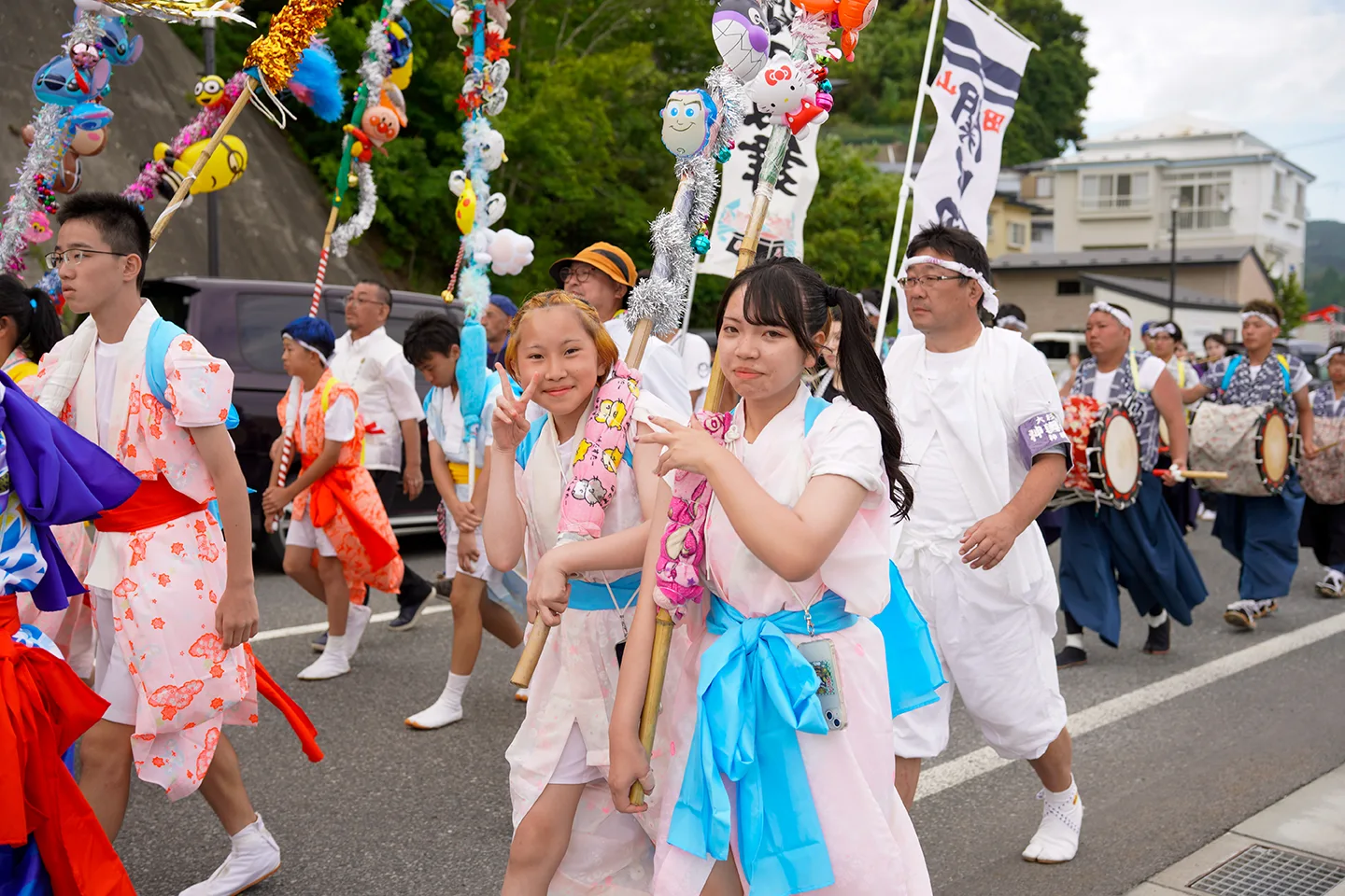 Girls in happi coats carrying decorated poles ahead of drummers at Yamada Matsuri