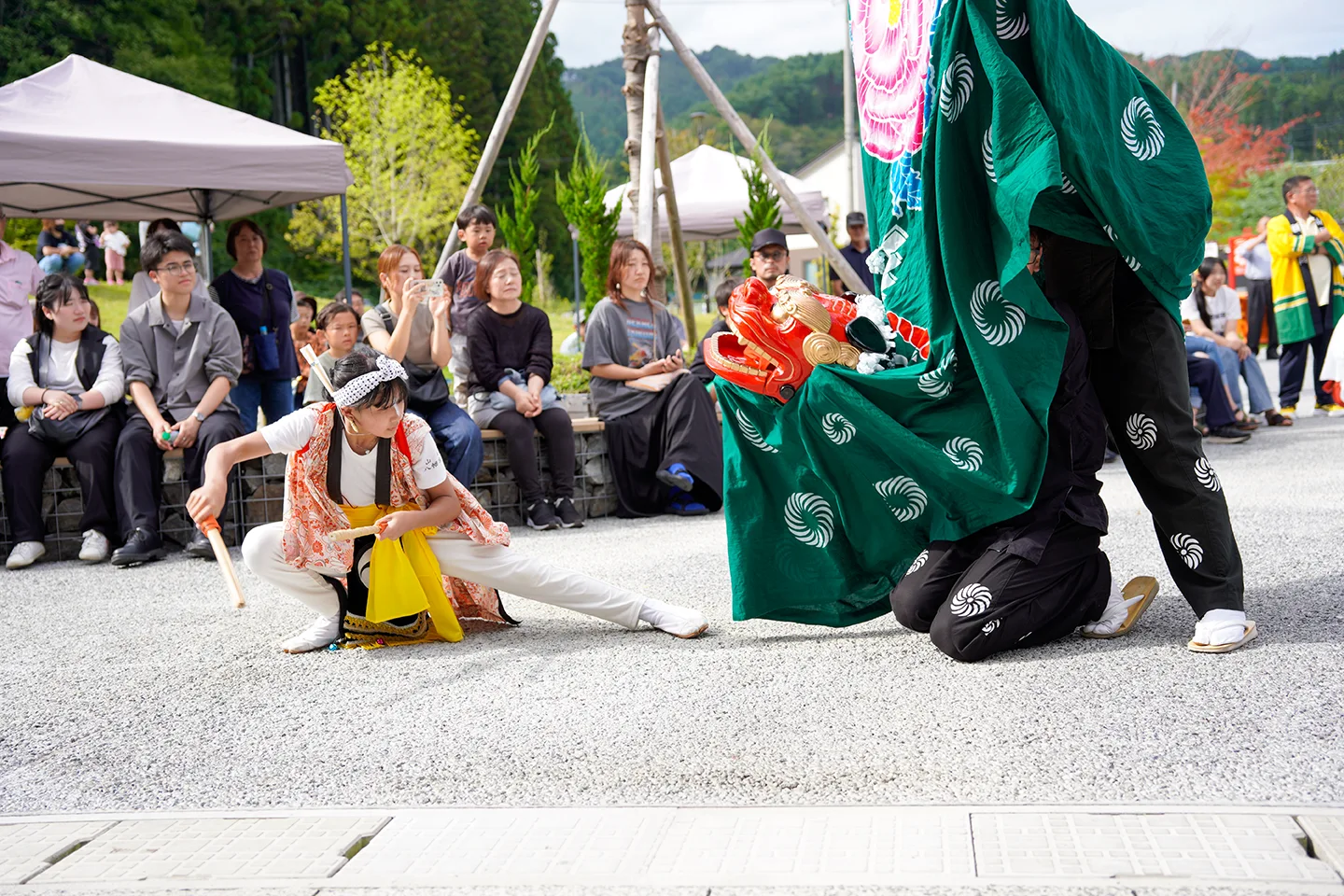 Girl with drumsticks facing a lion dancer at Yamada Matsuri