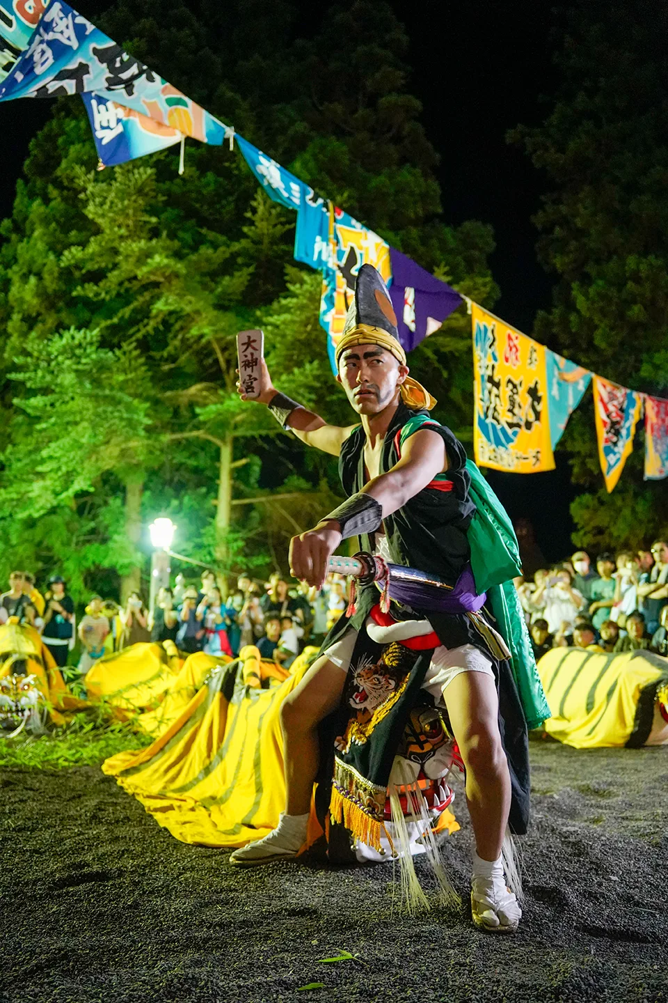 Performer in an eboshi hat striking a pose with Toramai tigers at night during Yamada Matsuri
