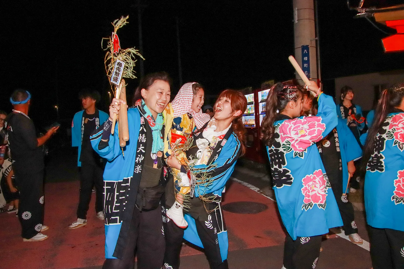 Hachiman Daikagura members laughing with lucky charms at night during Yamada Matsuri