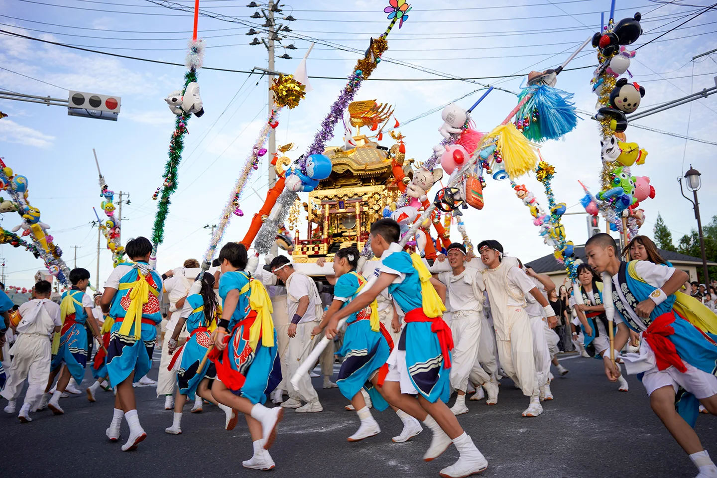 Children running alongside a portable shrine surrounded by decorated poles at Yamada Matsuri